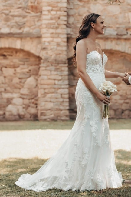 Vestido de novia largo color marfil con cola, estilo sirena, sin tirantes y encaje.