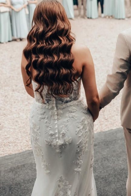 Vestido de novia largo color marfil con cola, estilo sirena, sin tirantes y encaje.