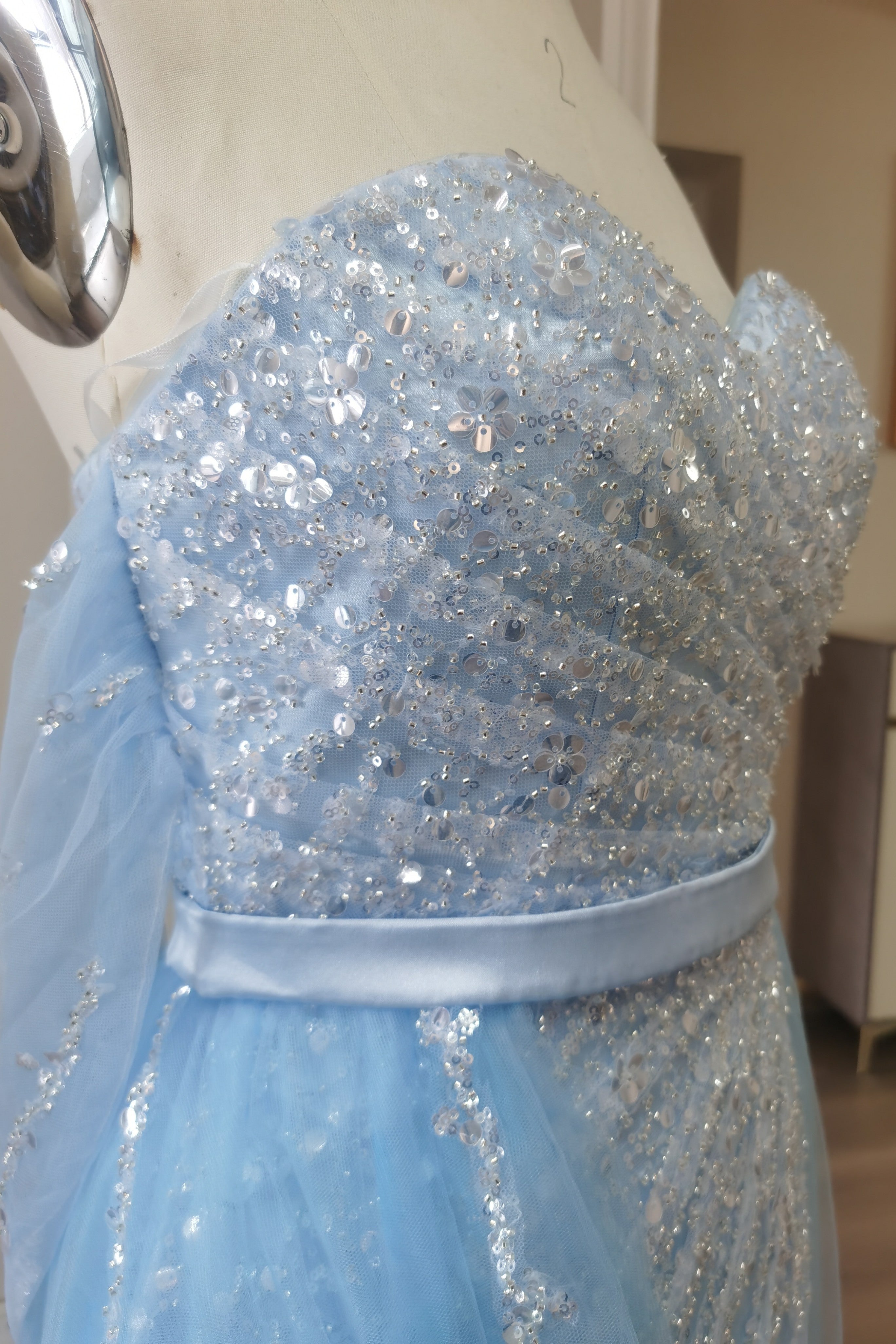 Abito da sera azzurro cielo con scollo a spalle scoperte e balze in tulle, decorato con paillettes