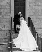 Bellissimi abiti da sposa bianchi in raso, linea a trapezio, scollo a barchetta, senza maniche, con volant e spacco frontale