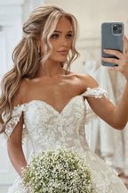 Belle robe de mariée princesse à encolure bardot, coupe évasée, ornée d'appliques, avec traîne