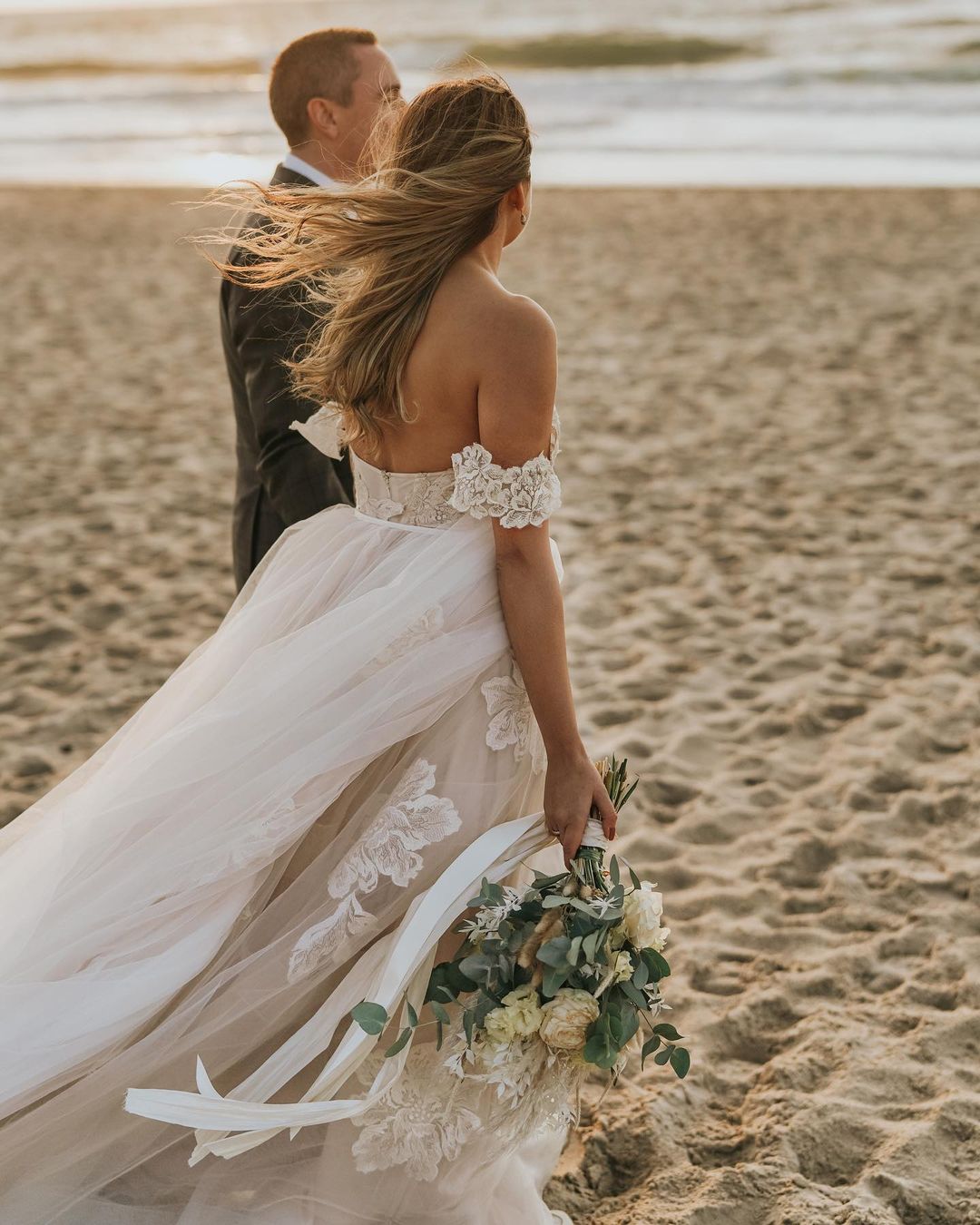 Robe de mariée longue en tulle avec dentelle appliquée, décolleté bardot et dos nu, coupe évasée